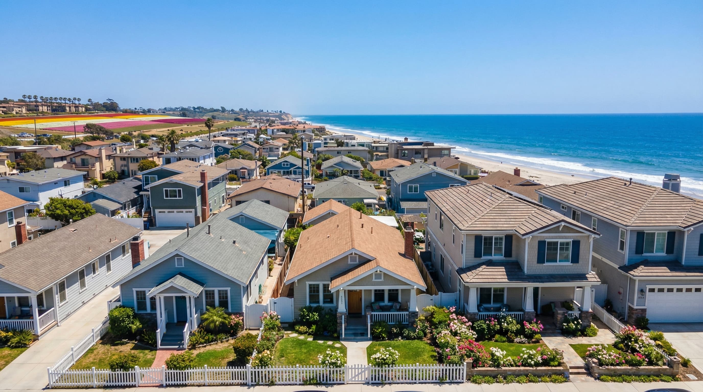 Charming Carlsbad California coastal village with beach cottages and family homes, flower fields visible in distance, and Pacific Ocean backdrop